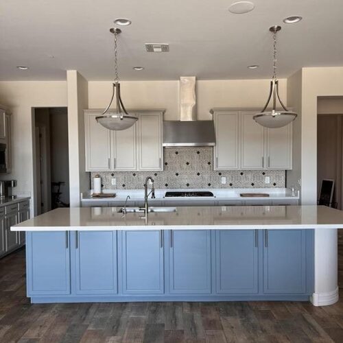 Modern Houston kitchen with refinished blue and white cabinets, sleek white countertops, mosaic backsplash, and pendant lights showcasing the Piper family's cabinet refinishing skills