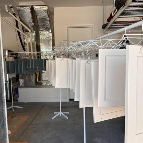 Workshop focused on Houston cabinets refinishing with painted white cabinet doors on drying racks, tools, and a professional setup for precision craftsmanship.