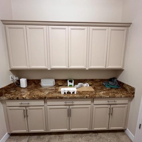 Cabinet refinishing project in Houston utility room showing cream-colored cabinets with metallic handles, stone countertop in earthy tones, organized decor, and neutral walls.