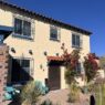 A Spanish-style house with stucco walls, terracotta roof tiles, desert landscaping, vibrant bougainvillea, turquoise chairs, and wrought iron accents in Tucson's arid environment.