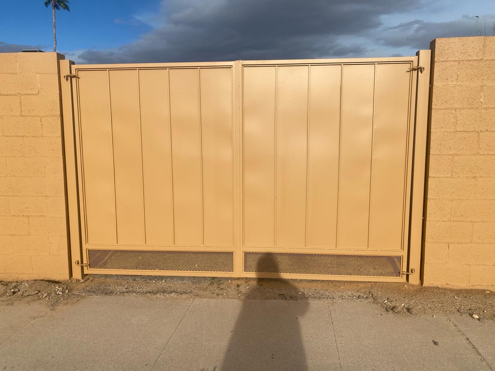Freshly painted beige metal gate and fence in Tucson showcases expert gate and fence painting in Tucson, blending with brick wall and desert landscape.