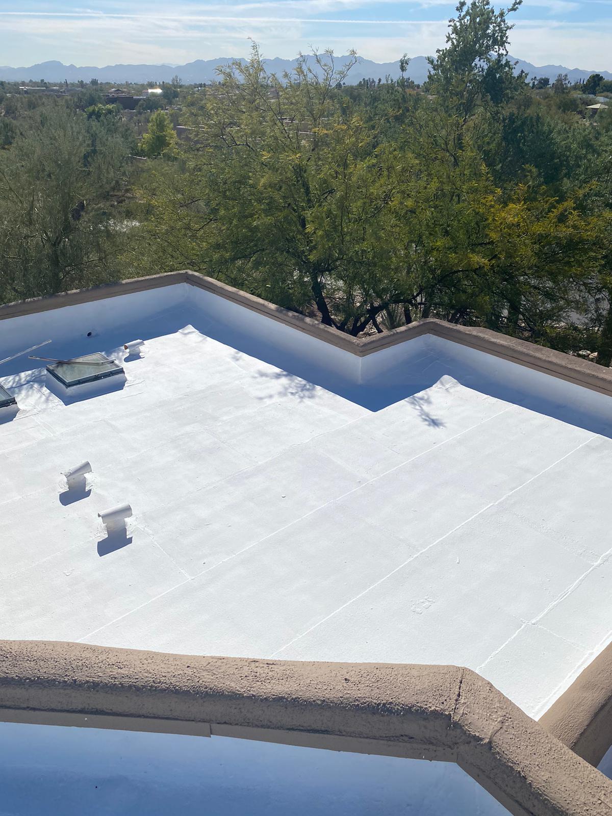White roof coatings applied by Piper Family Painting Company enhance energy efficiency and protection on a flat rooftop surrounded by greenery and mountains.