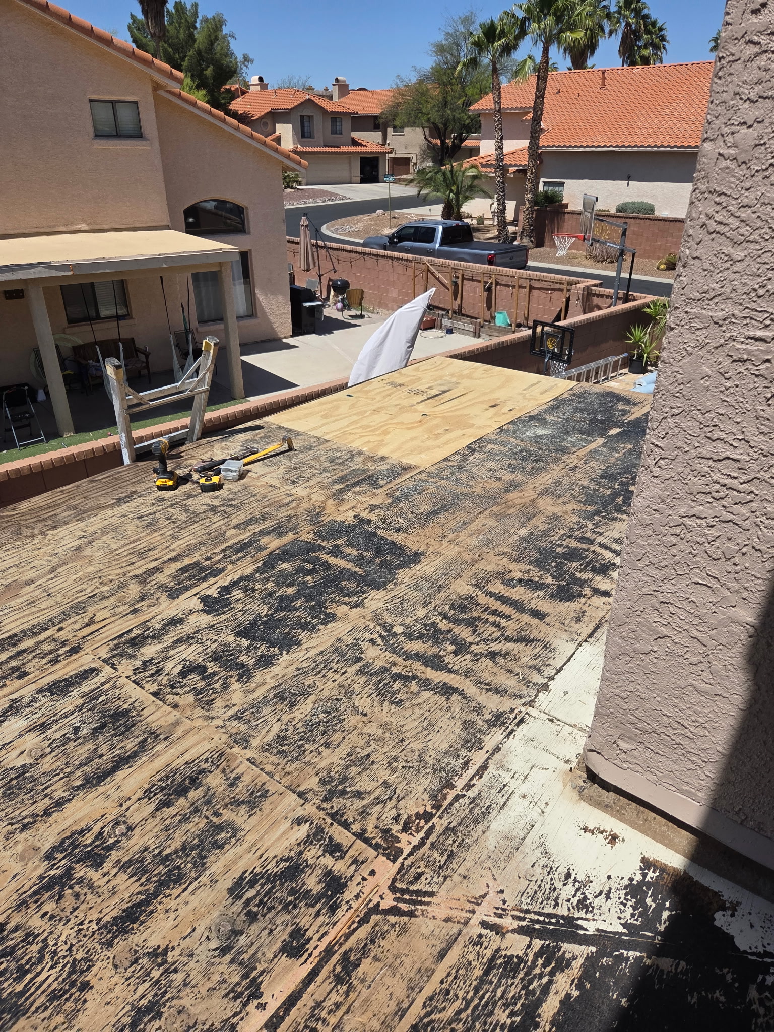 Roof coatings prep underway by Piper Family Painting Company, showing stripped roofing, tools, and suburban homes in a sunny, UV-prone environment.