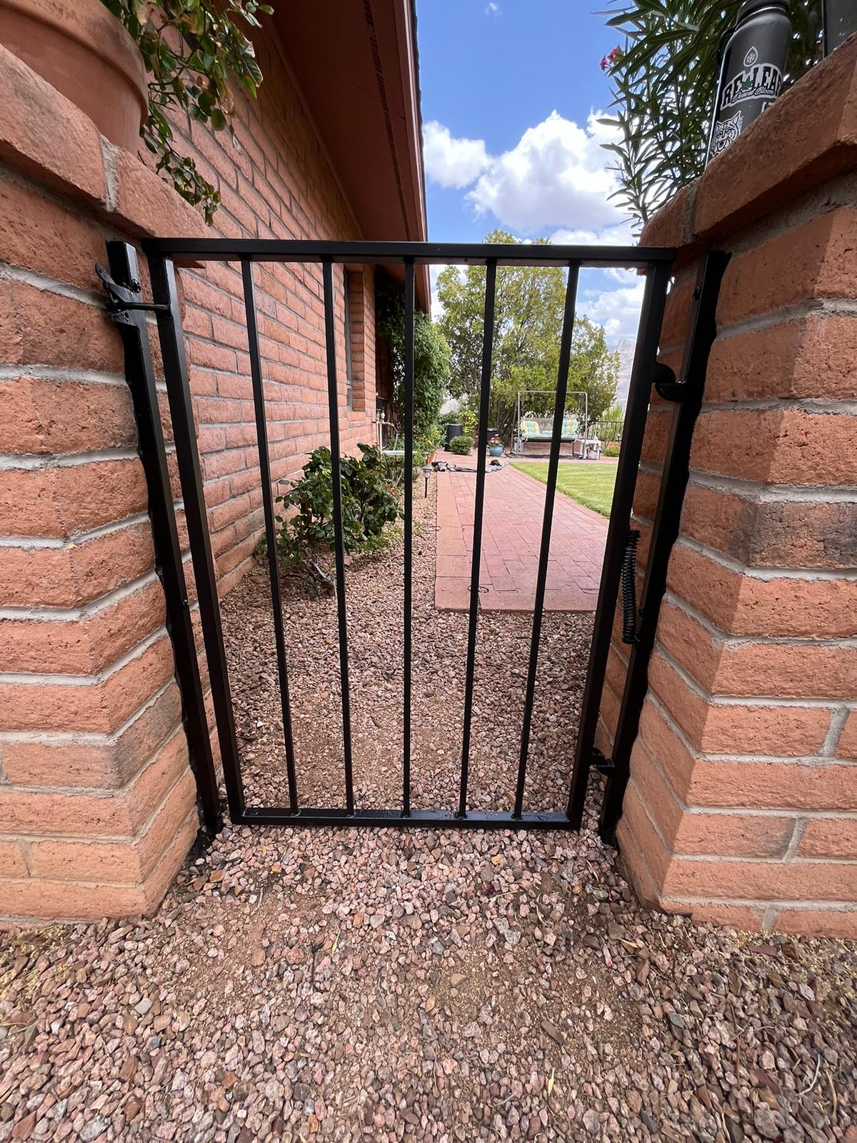 Dove Mountain Painting Company work by Piper Family Painting Company featuring a painted black gate, brick pillars, and lush landscaping in natural light.