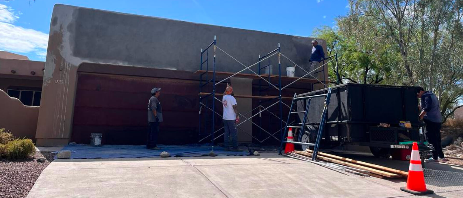 Piper Family Painting Company worker from Marana Painting Company prepares a home's exterior for repainting, standing on scaffold under a clear blue sky.