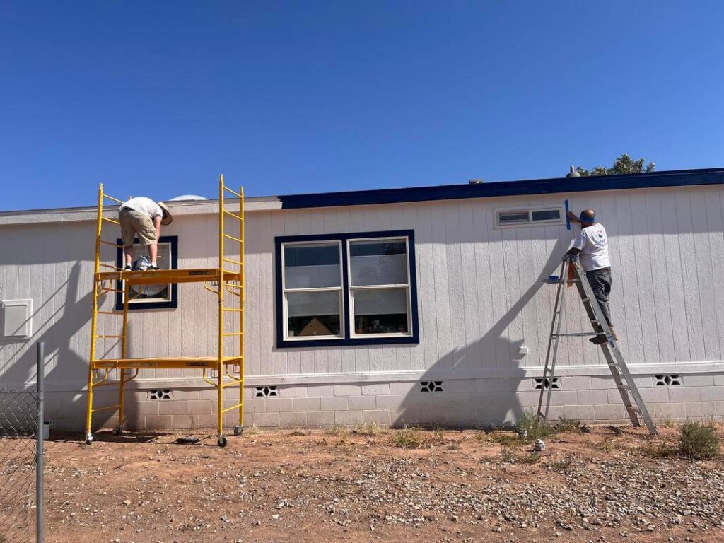 Piper Family Painting Company workers from Oro Valley Painting Company paint white exterior and blue trim on a home under a clear sky with clean, professional precision.