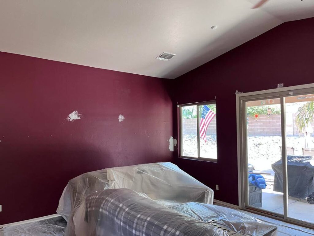 Room prep by Piper Family Painting Company, an Oro Valley Painting Company, showing burgundy walls, white spackle, and covered furniture under natural light.