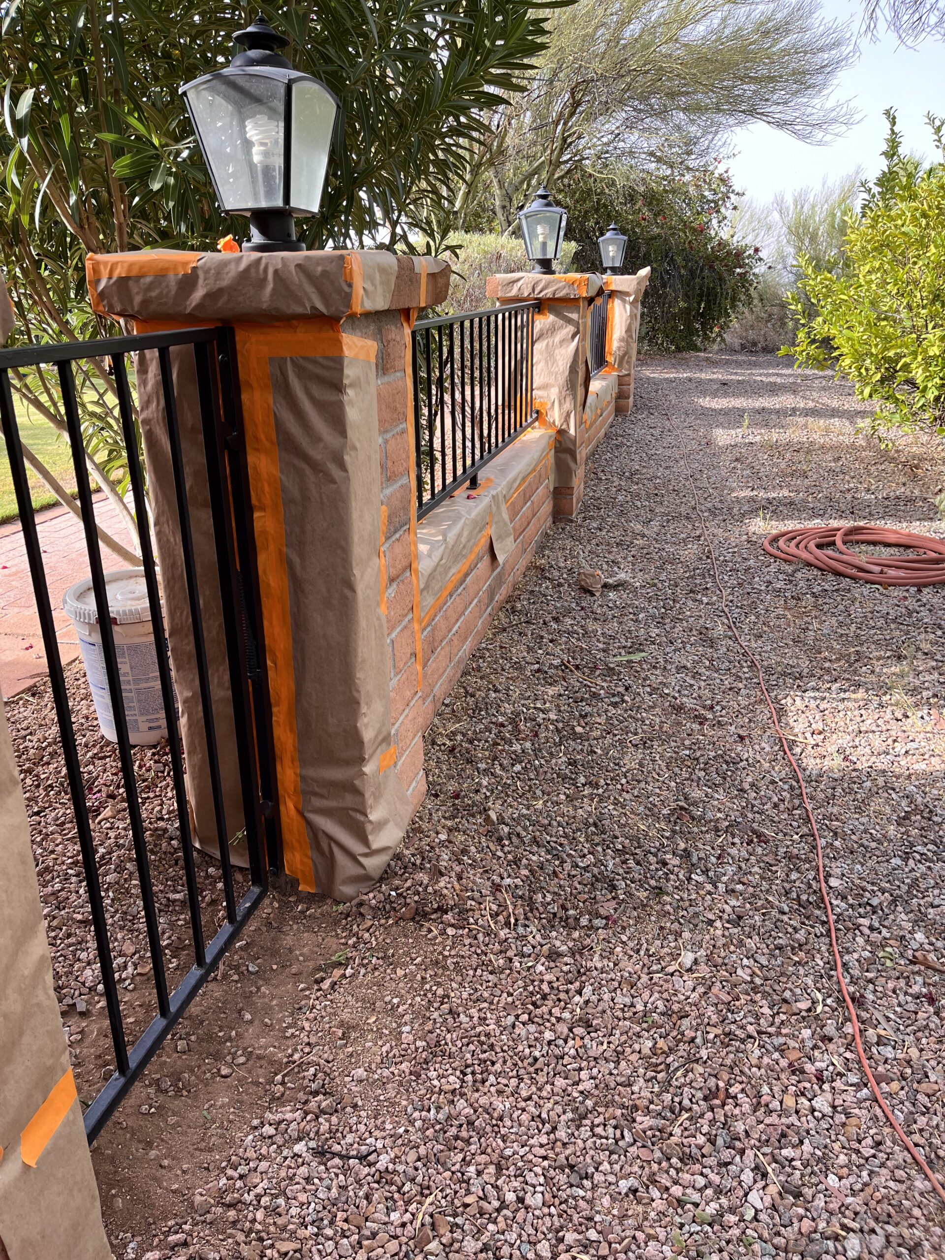 Piper Family Painting Company prepares a brick and metal fence in Rancho Vistoso with meticulous masking, showcasing their detail-focused painting services.