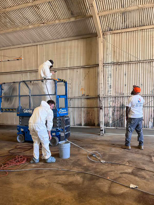 Piper Family Painting Company team from Rancho Vistoso painting interior of industrial warehouse using lifts and spray equipment, showing skill and safety.