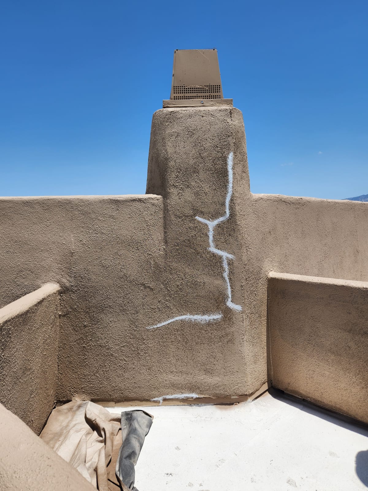 Piper Family Painting Company stucco repair in progress showing a beige wall with a vertical crack marked for restoration under a clear blue sky.